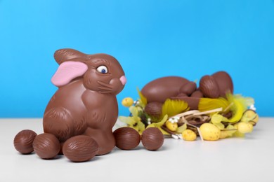 Photo of Chocolate Easter bunny and eggs on white table against light blue background