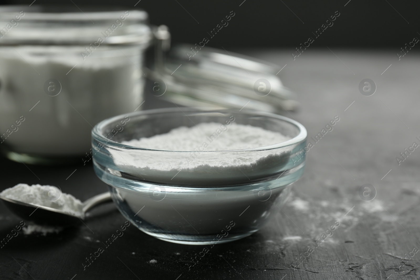 Photo of Baking powder in bowl and spoon on black textured table, closeup. Space for text