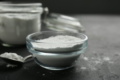 Photo of Baking powder in bowl and spoon on black textured table, closeup. Space for text