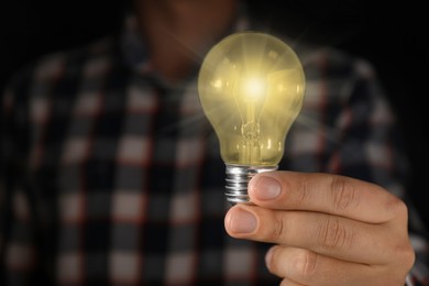 Image of Man holding glowing light bulb in darkness, closeup. Space for text