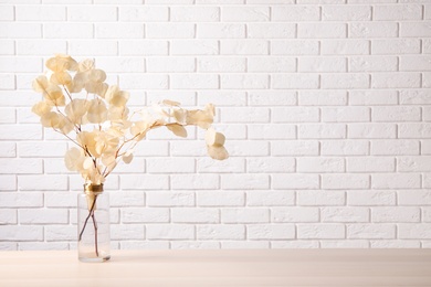 Dried eucalyptus branches in vase on table against white brick wall. Space for text