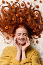 Photo of Beautiful redhead woman with flowers in hair lying on white plaid, top view