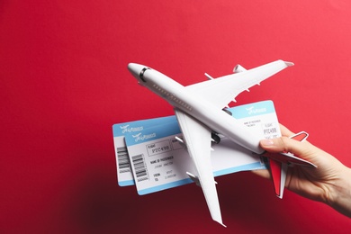 Photo of Woman holding toy airplane and tickets on red background, closeup