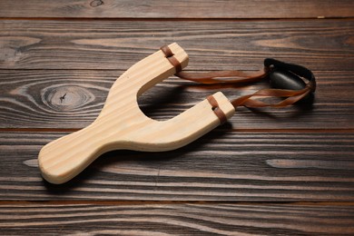 Slingshot with leather pouch and pebble on wooden table