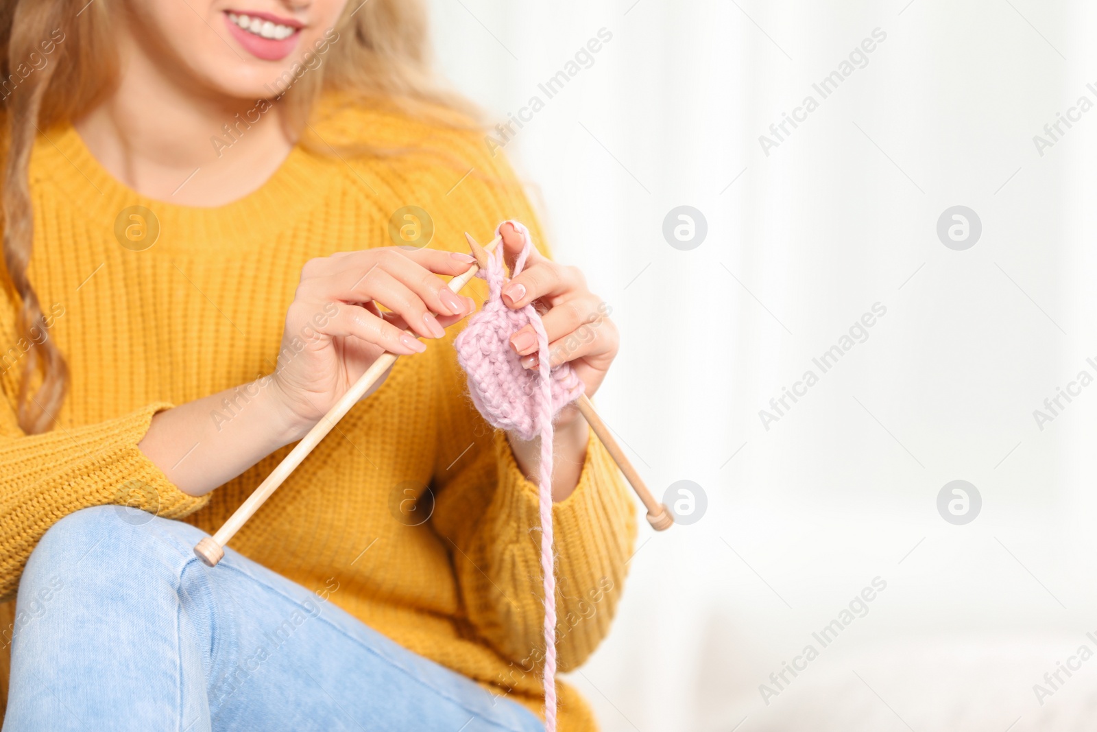 Photo of Young woman in cozy warm sweater knitting with needles on light background. Space for text