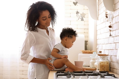 Photo of African-American woman with her baby in kitchen. Happiness of motherhood