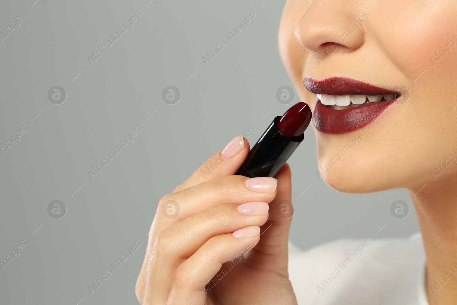 Photo of Beautiful woman applying dark lipstick on gray background, closeup. Space for text