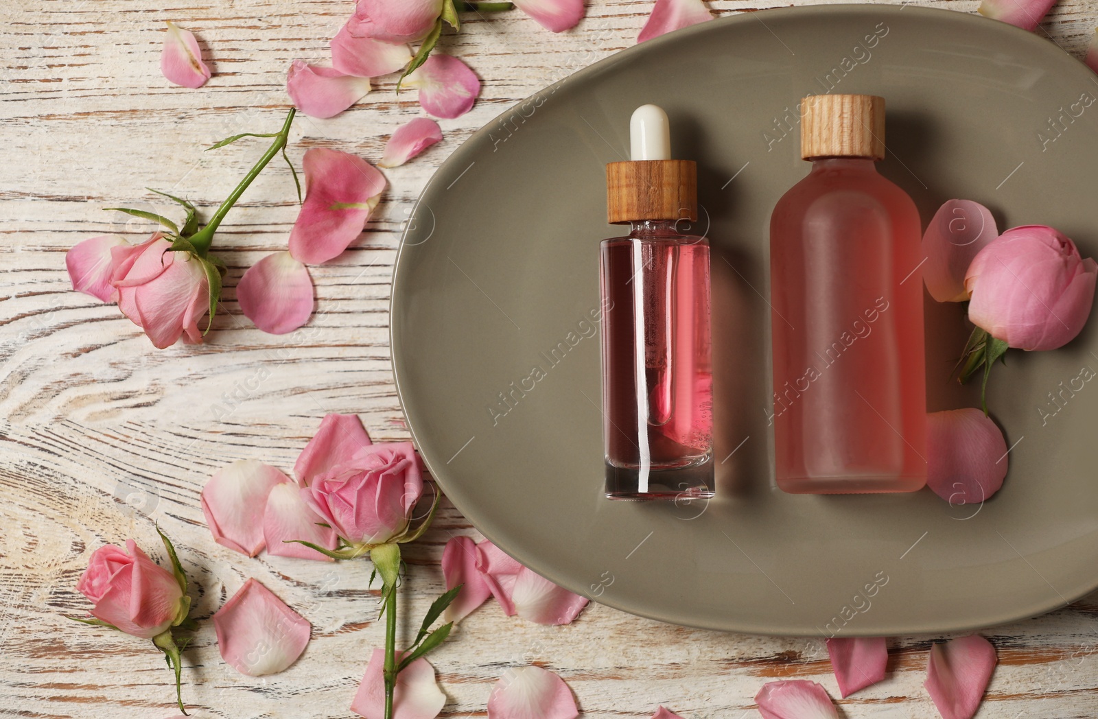 Photo of Flat lay composition with essential rose oil and flowers on white wooden table