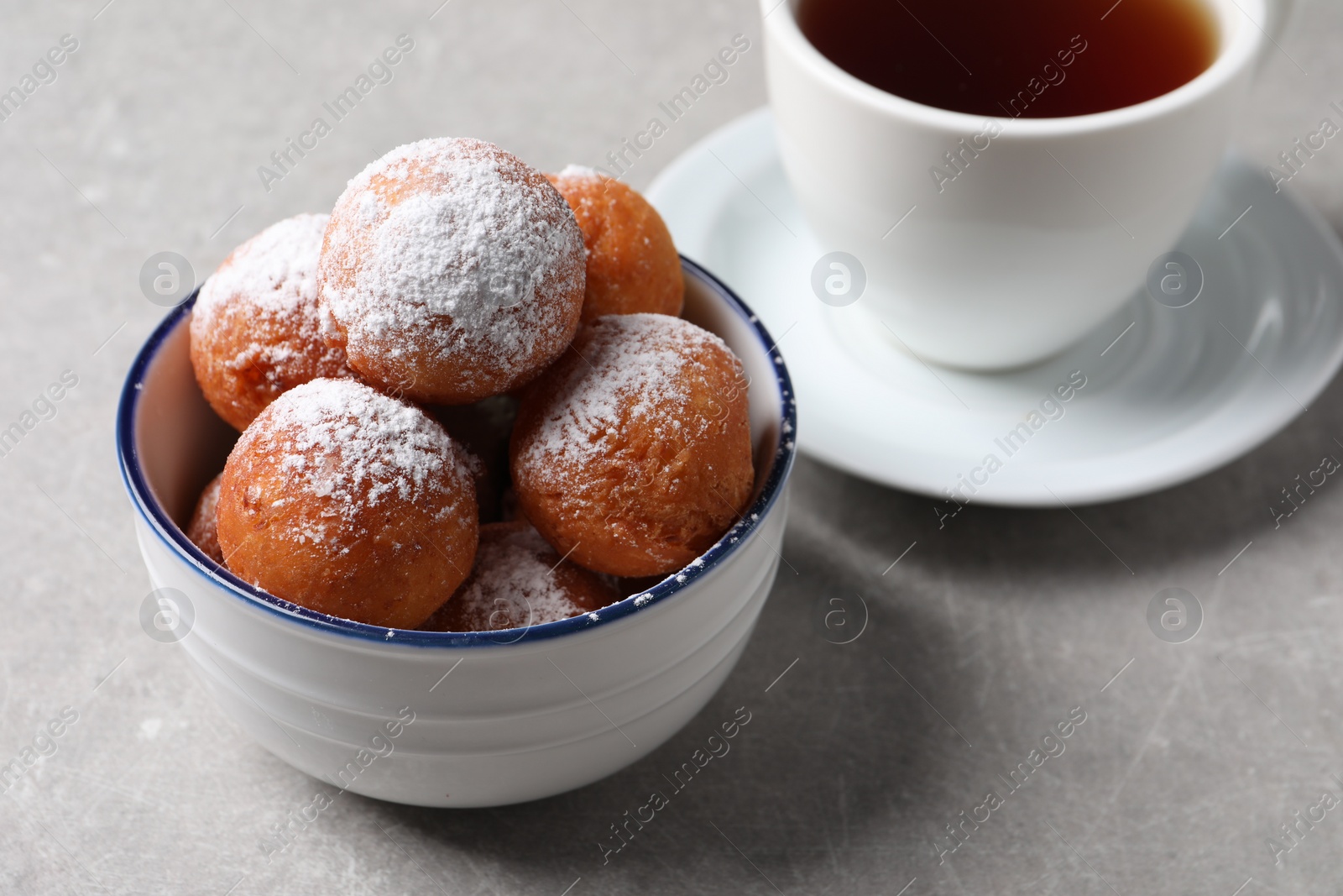 Photo of Delicious sweet buns in bowl and cup of tea on gray table, closeup