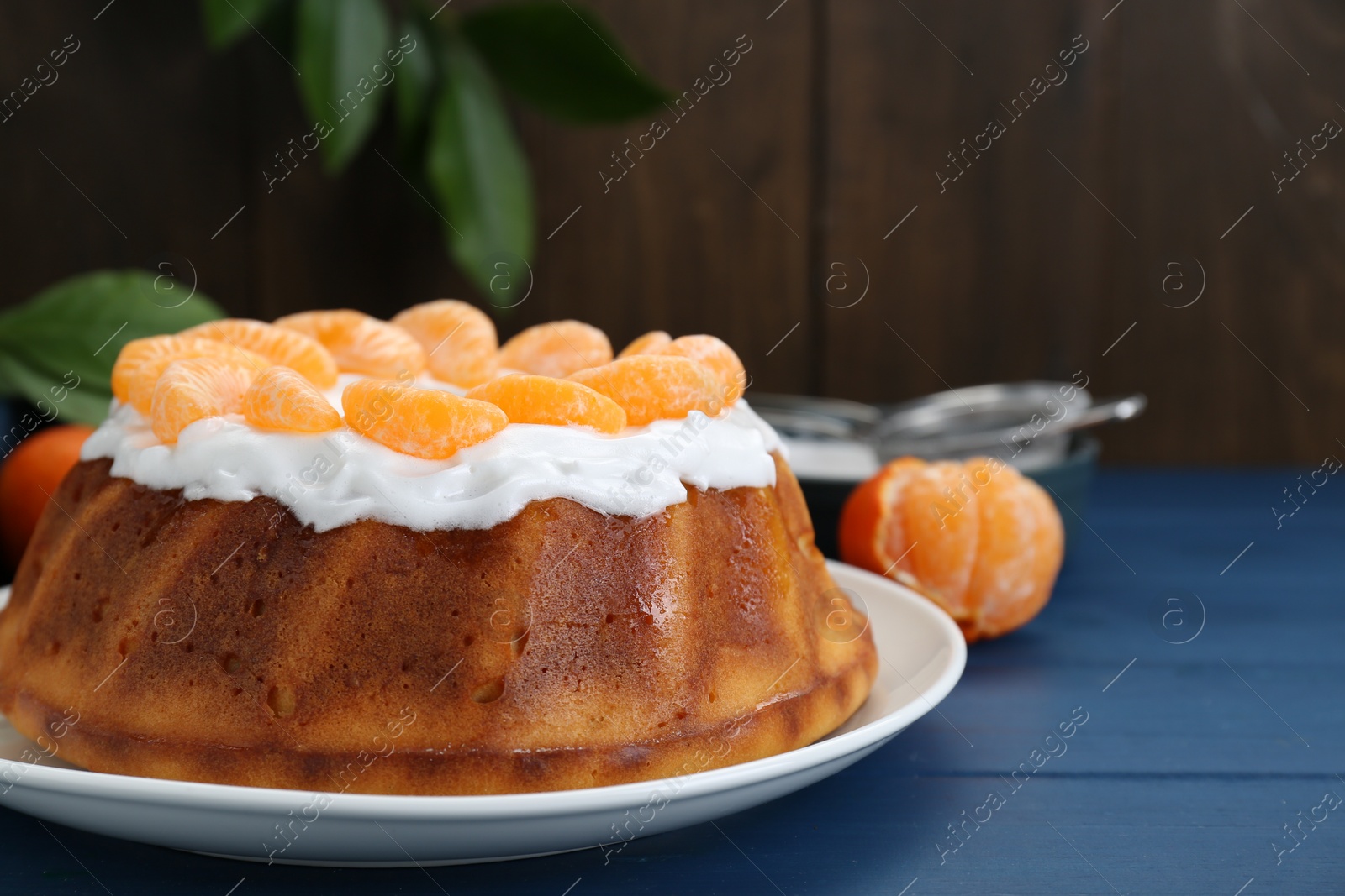 Photo of Homemade yogurt cake with tangerines and cream on blue wooden table. Space for text