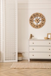 Stylish room with wooden folding screen and chest of drawers near white wall. Interior design