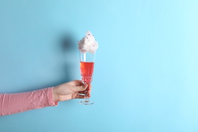 Photo of Woman holding glass of cotton candy cocktail on light blue background, closeup. Space for text