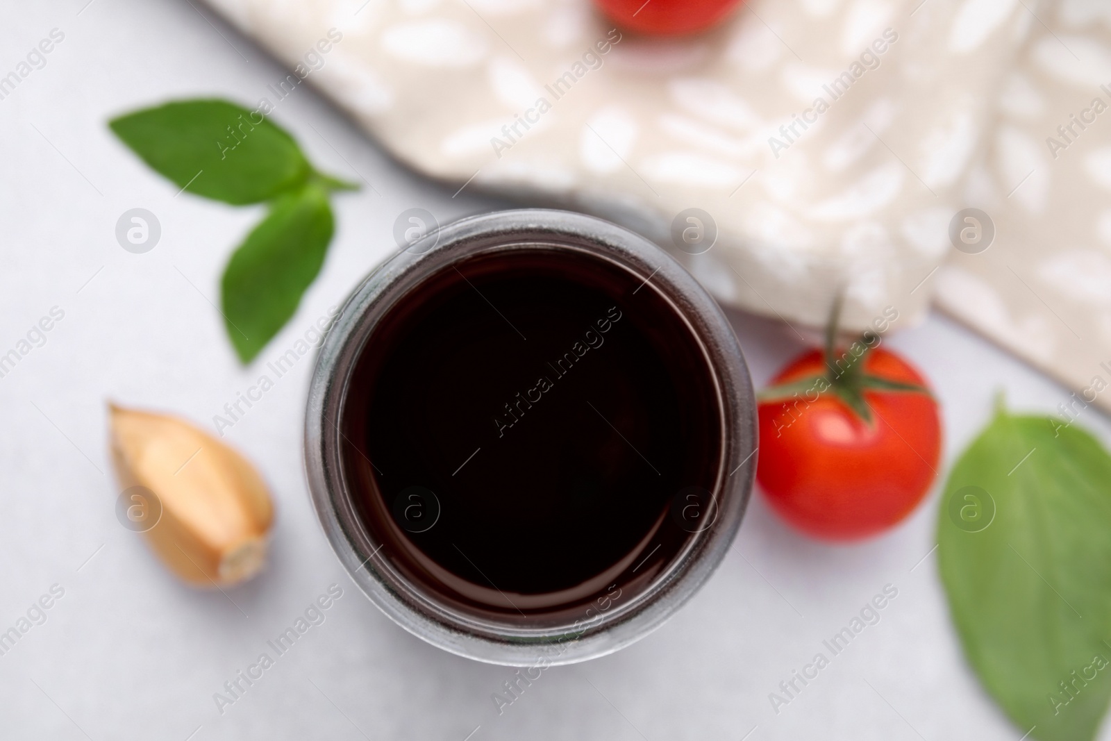 Photo of Balsamic vinegar, basil, tomato and garlic on white table, top view