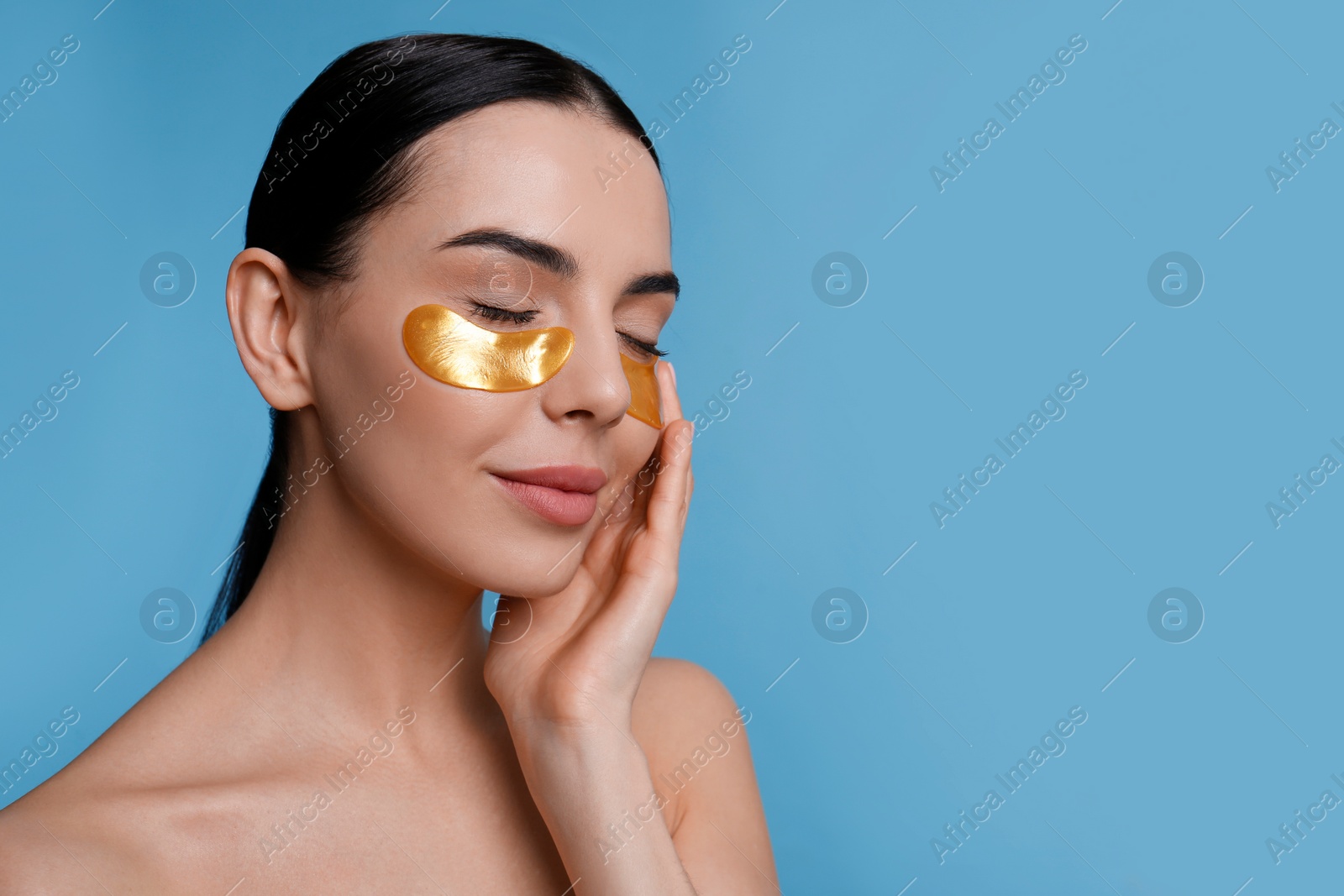 Photo of Beautiful young woman with under eye patches on light blue background, space for text