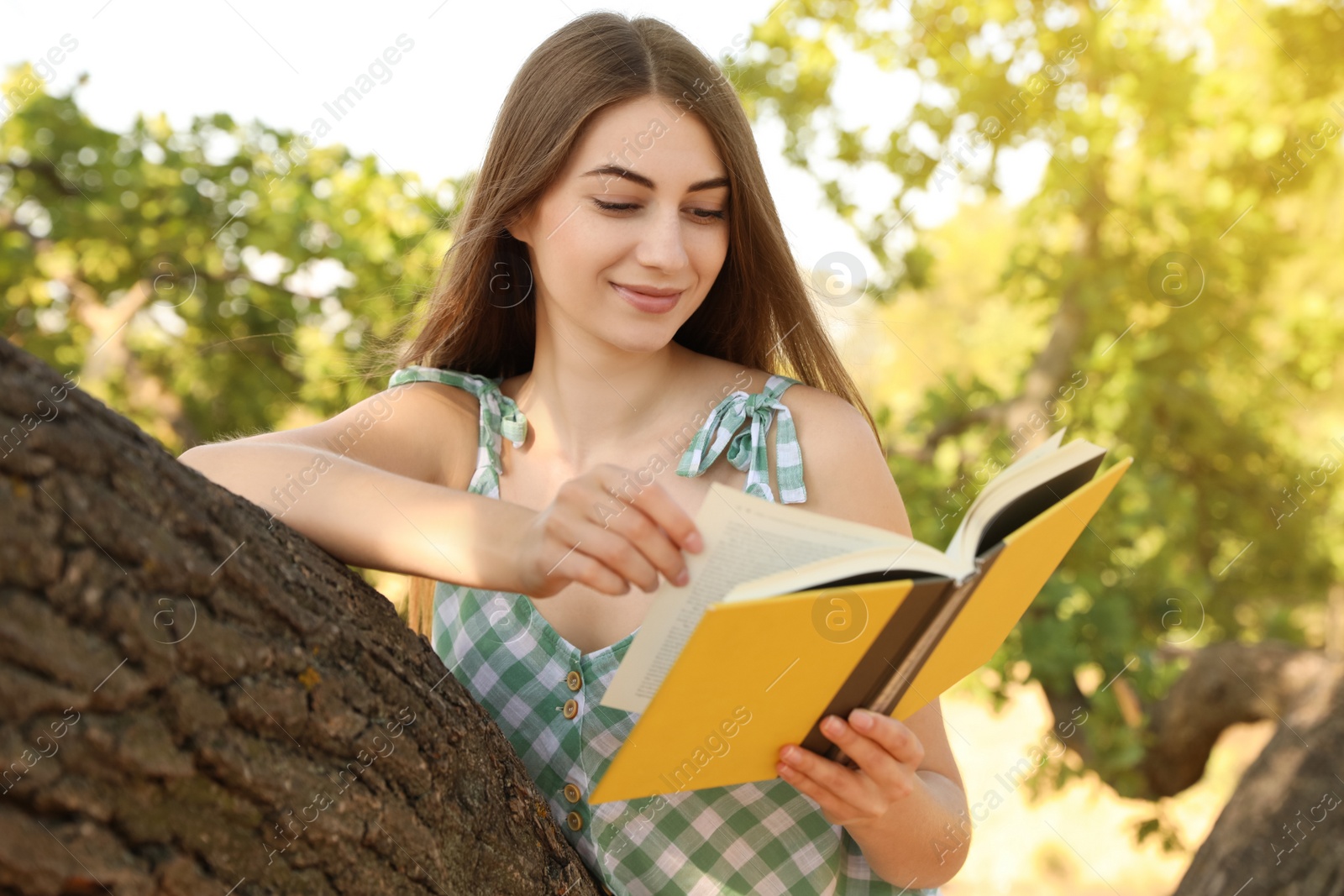 Photo of Young woman reading book on tree in park