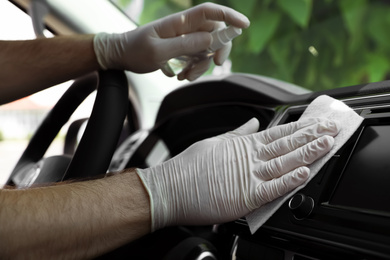 Photo of Man cleaning dashboard with wet wipe and antibacterial spray in car, closeup