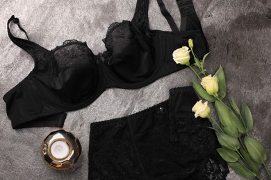 Photo of Elegant black plus size women's underwear, candle and beautiful eustoma flowers on grey background, flat lay