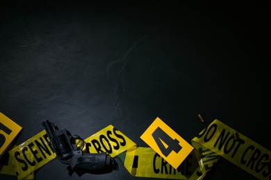 Photo of Flat lay composition with gun and crime scene marker on black slate background. Space for text