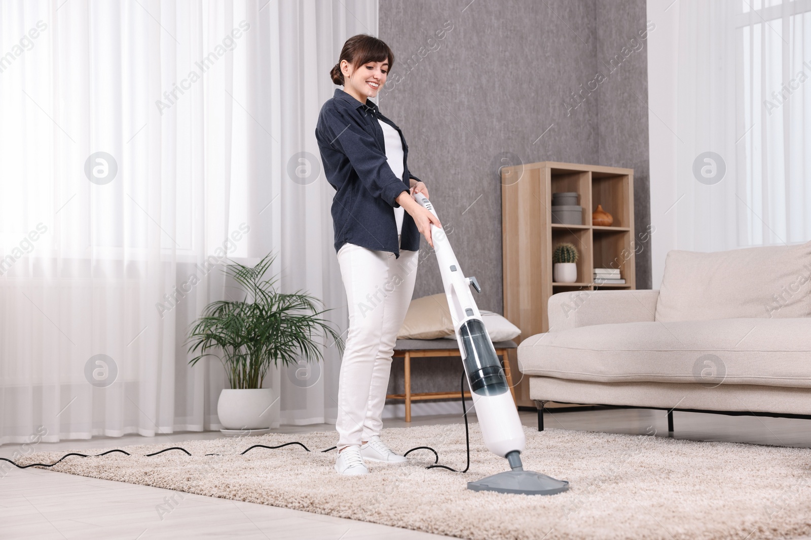 Photo of Happy young housewife vacuuming carpet at home