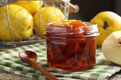 Tasty homemade quince jam in jar, spoon and fruits on wooden table, closeup