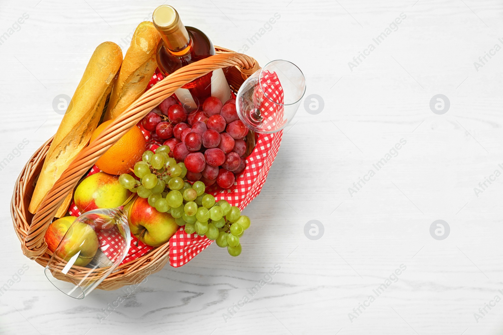 Photo of Picnic basket with products and wine on white wooden table, top view. Space for text