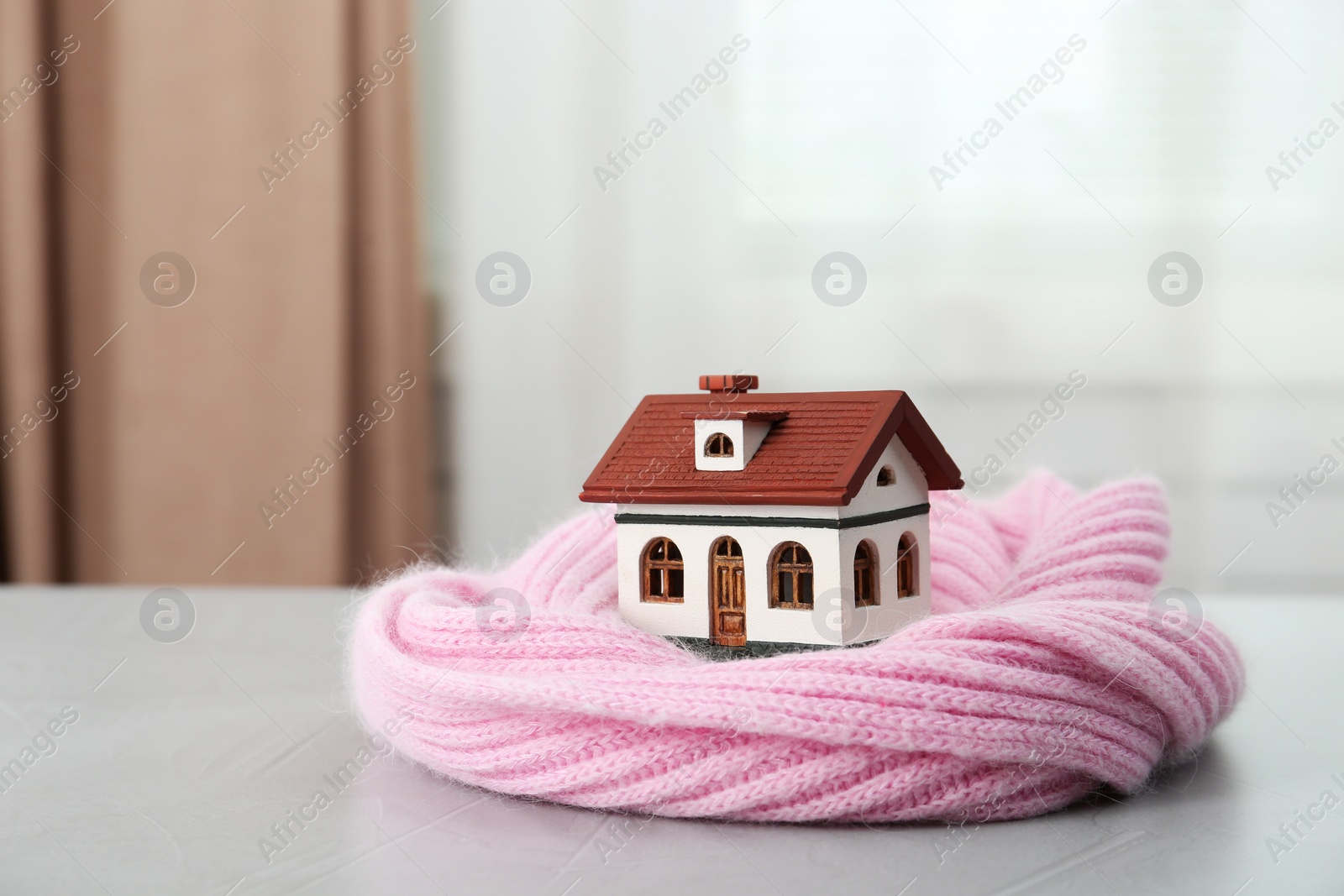 Photo of Wooden house model and scarf on grey table indoors. Heating efficiency