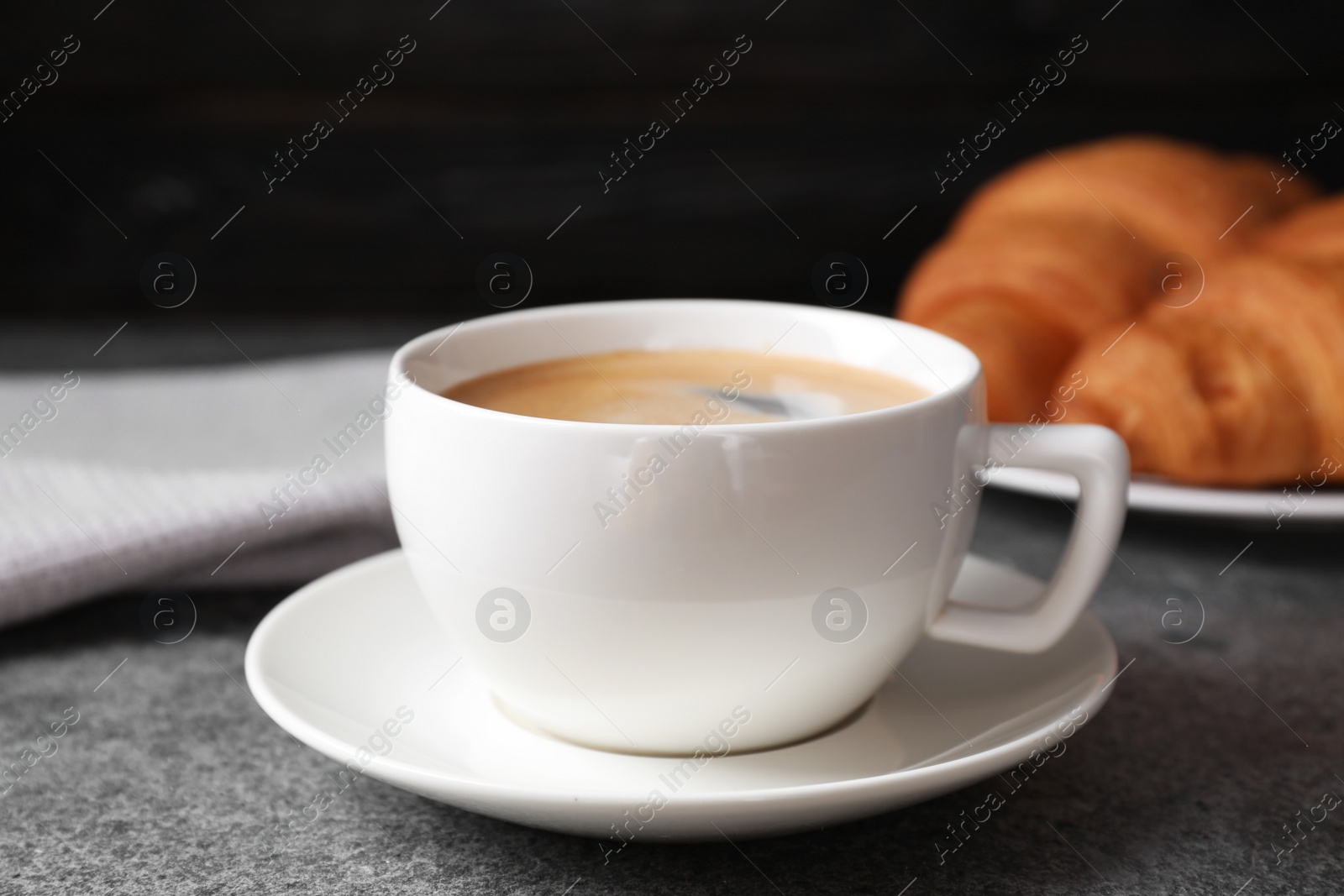 Photo of Tasty fresh croissants and coffee on grey table, closeup