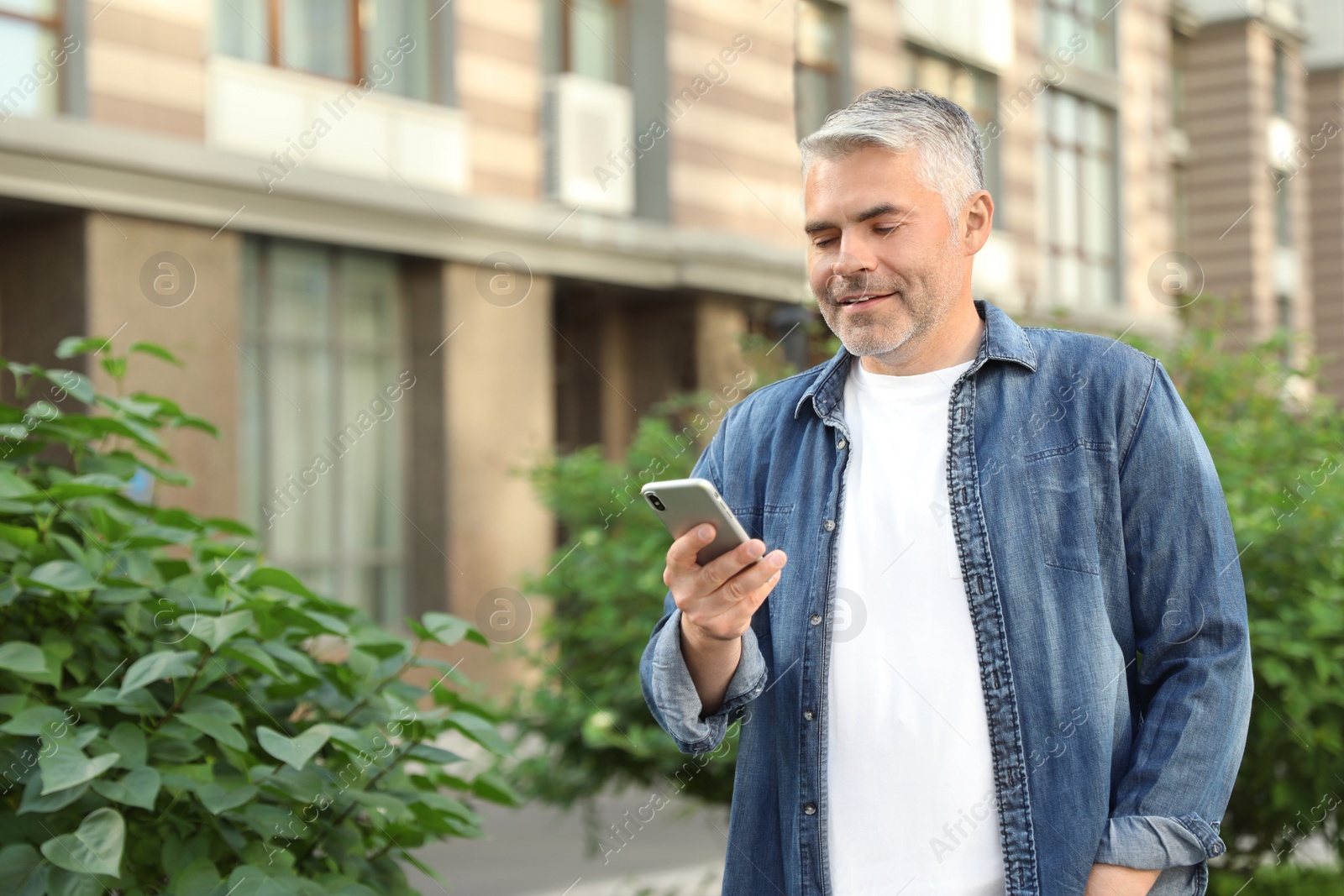 Photo of Portrait of handsome mature man using mobile phone in city. Space for text