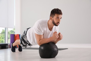 Athletic man doing plank exercise with medicine ball in modern gym