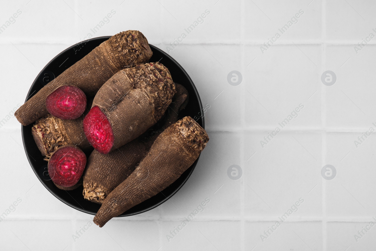 Photo of Whole and cut red beets in bowl on white table, top view. Space for text