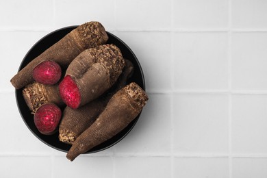 Photo of Whole and cut red beets in bowl on white table, top view. Space for text