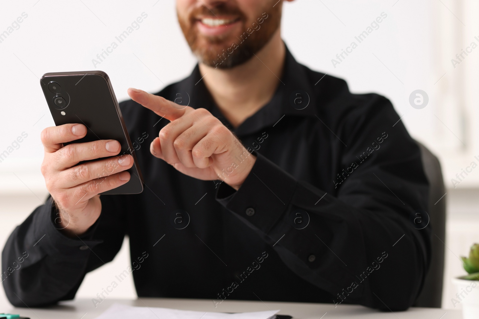 Photo of Smiling man using smartphone at table in office, closeup