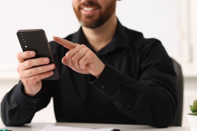 Smiling man using smartphone at table in office, closeup