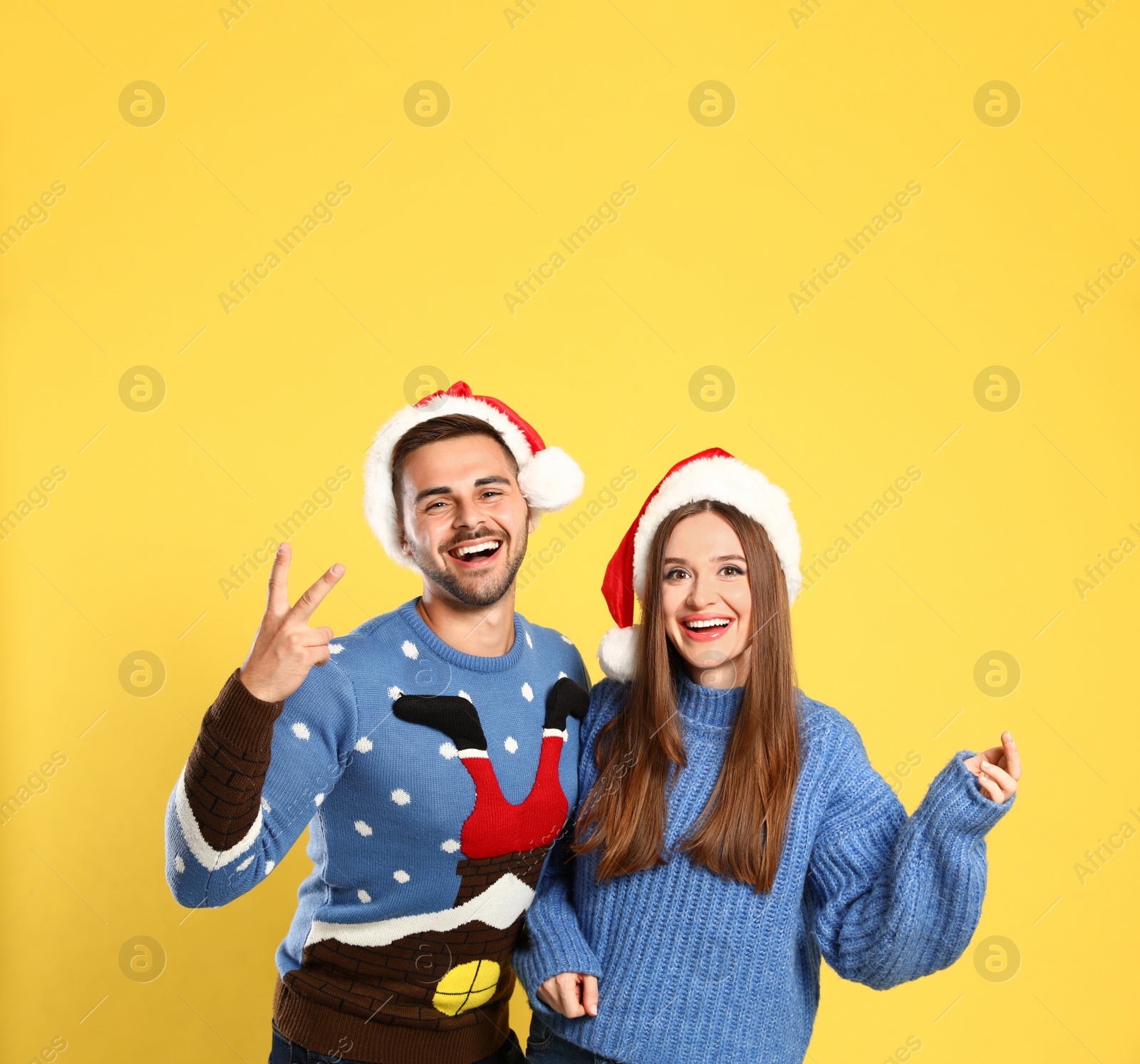 Photo of Couple wearing Christmas sweaters and Santa hats on yellow background