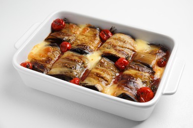 Tasty eggplant rolls with tomatoes and cheese in baking dish on white table, closeup