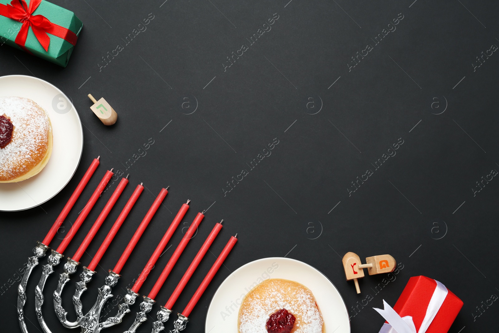 Photo of Hanukkah traditional menorah, candles, doughnuts, dreidels with letters He, Pe, Nun, Gimel on black background, flat lay. Space for text