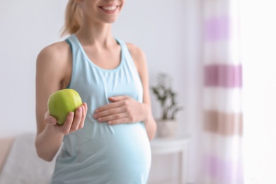 Photo of Young pregnant woman holding apple at home