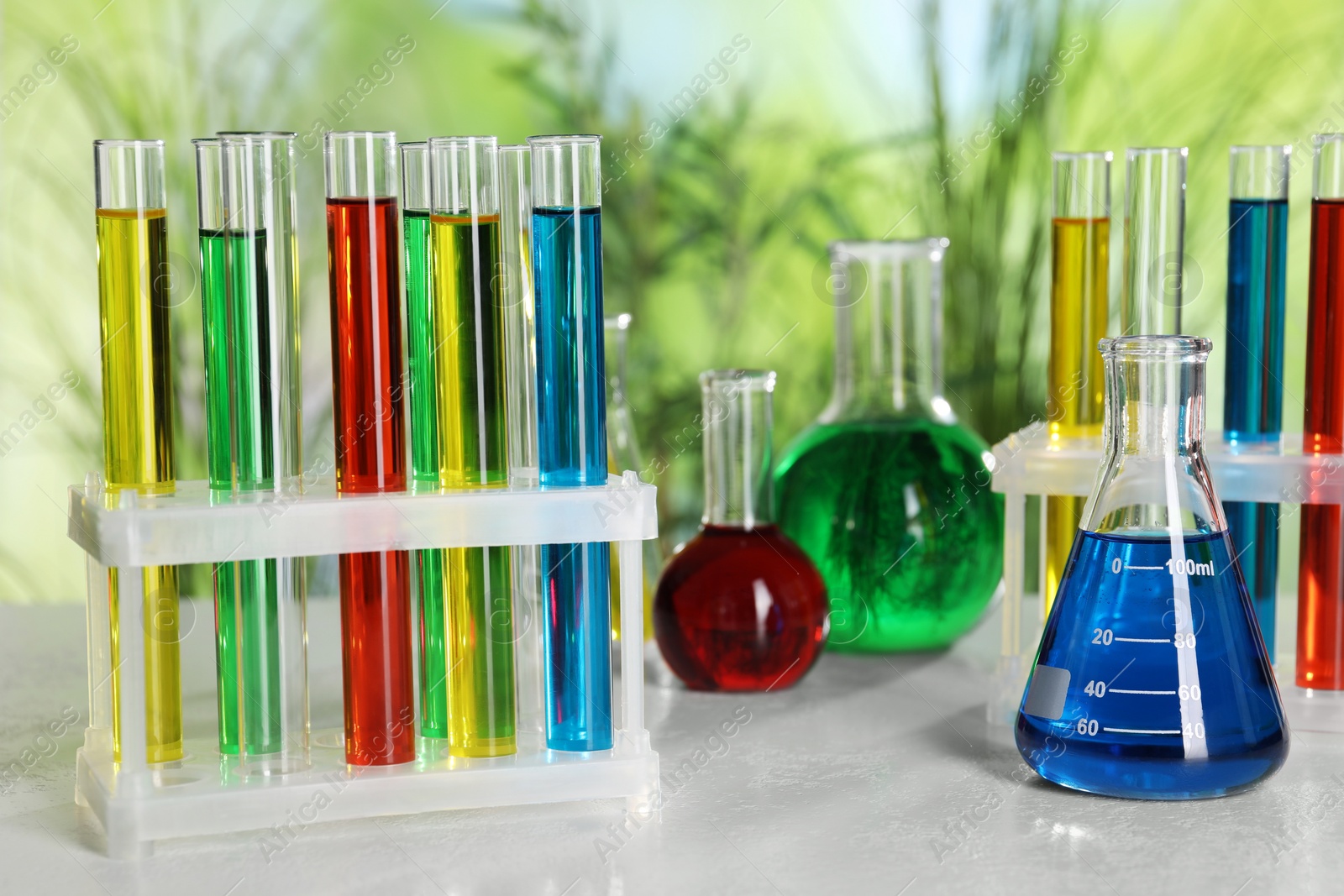 Photo of Test tubes with liquids in stand and flasks on table against blurred background