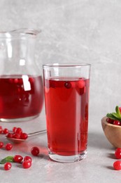Photo of Tasty cranberry juice in glass and fresh berries on light grey table