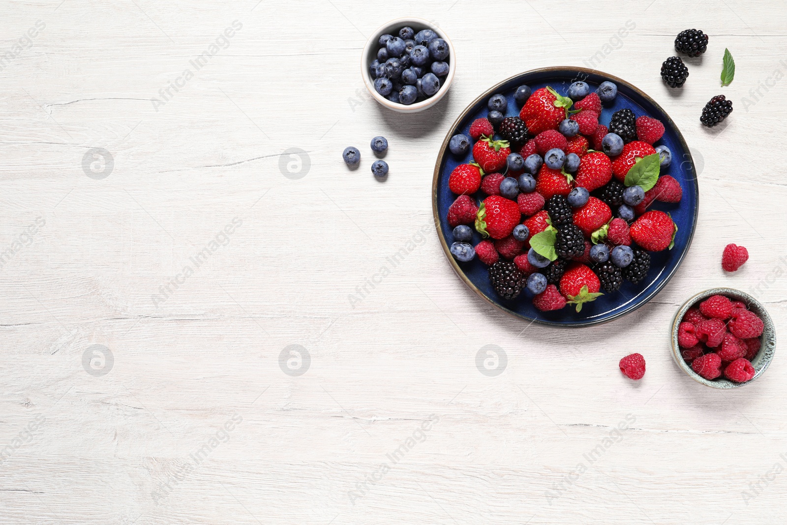 Photo of Different fresh ripe berries on light wooden table, flat lay. Space for text