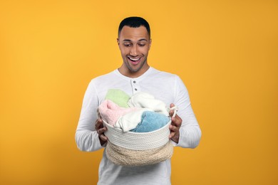 Photo of Emotional man with basket full of laundry on orange background