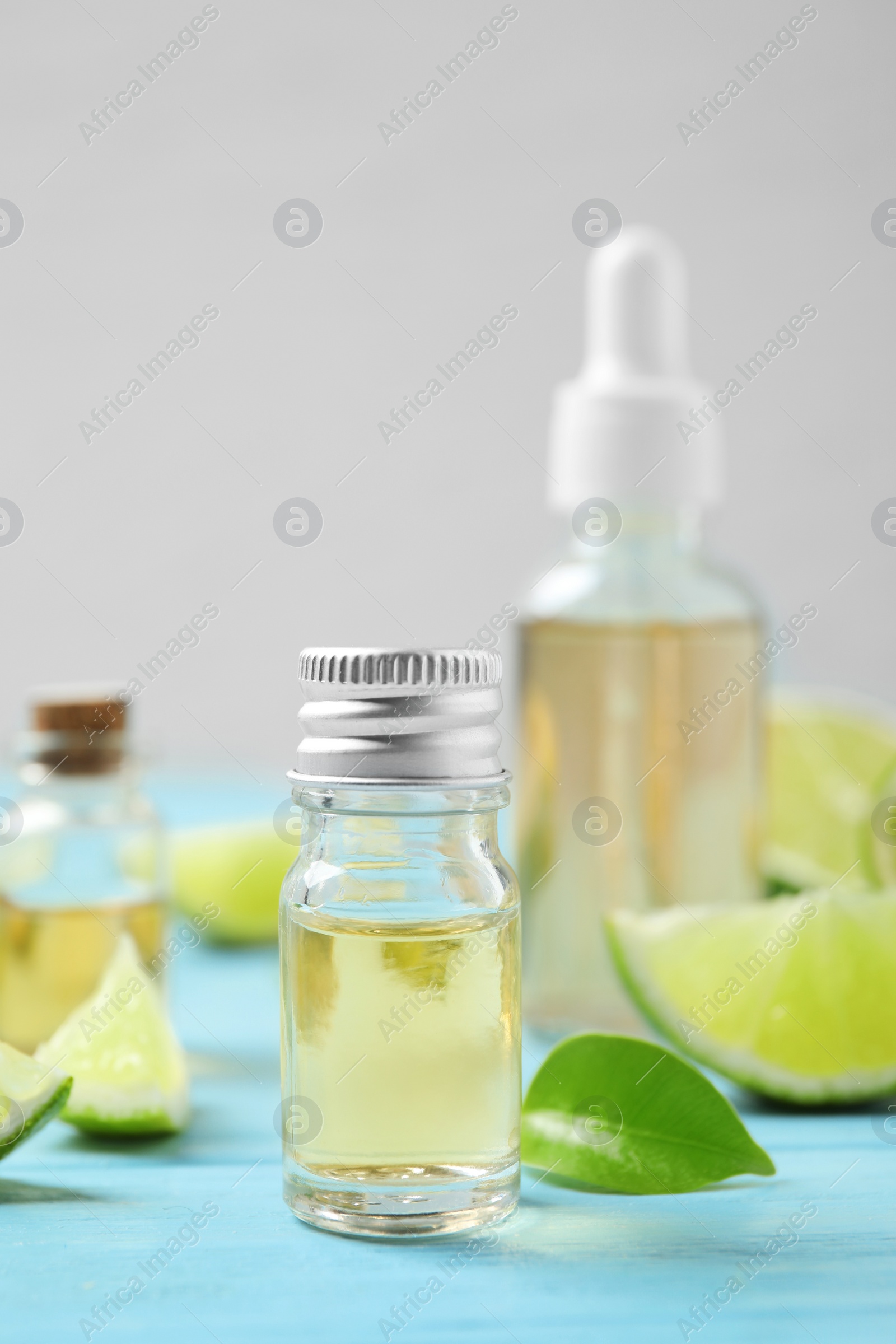 Photo of Lime essential oil and cut citrus fruits on light blue wooden table