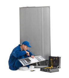 Male technician repairing refrigerator on white background