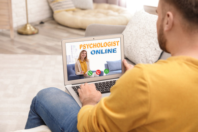 Image of Man using laptop at home for online consultation with psychologist via video chat, focus on screen