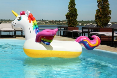 Photo of Funny inflatable unicorn ring floating in swimming pool on sunny day, outdoors