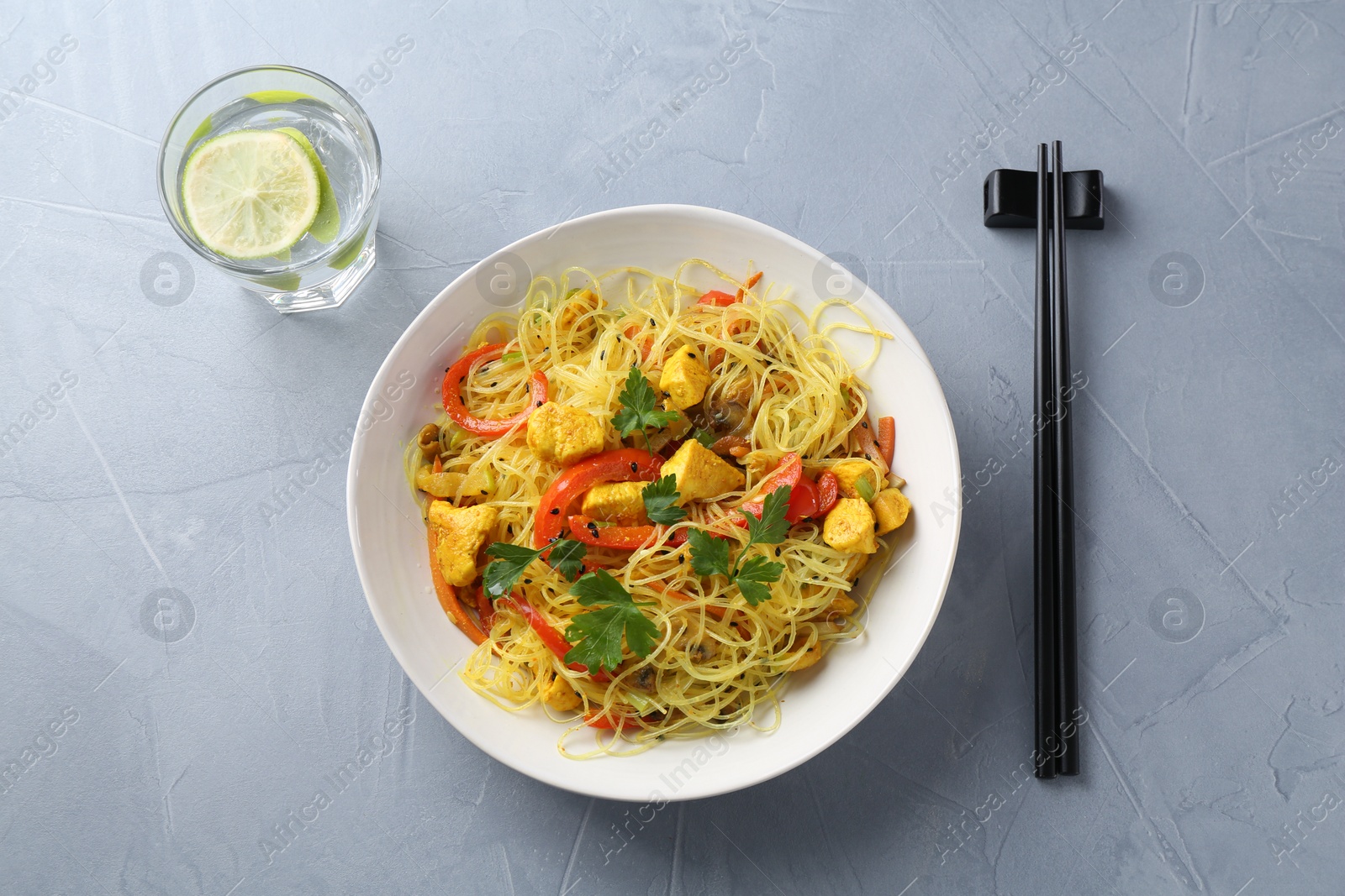 Photo of Stir-fry. Delicious cooked noodles with chicken and vegetables in bowl served on gray textured table, flat lay