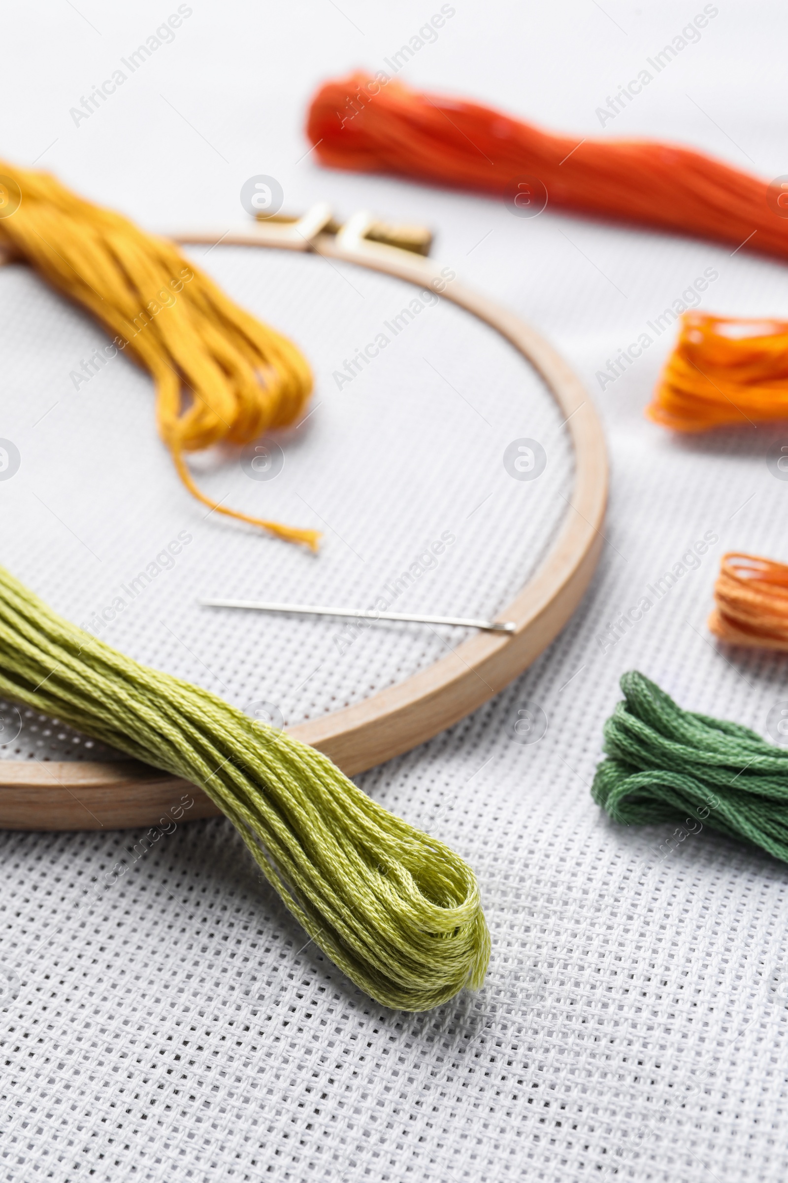 Photo of Threads near embroidery hoop with white fabric, closeup