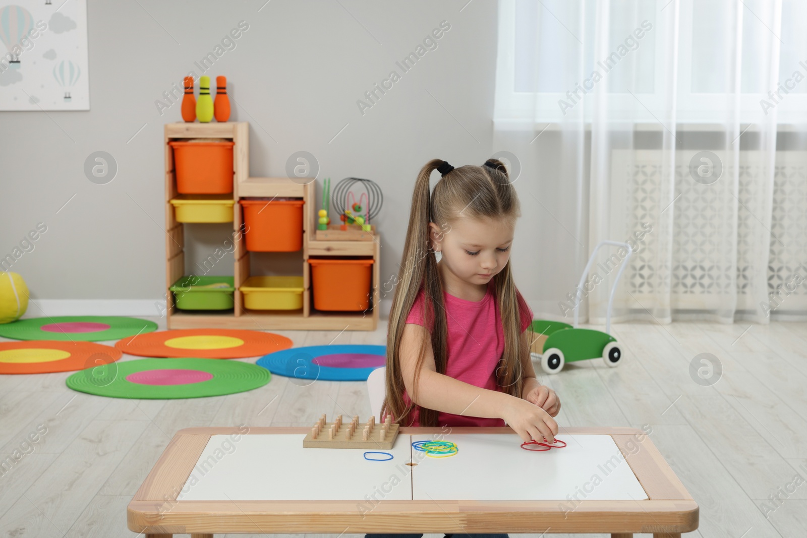Photo of Motor skills development. Girl playing with geoboard and rubber bands at white table in kindergarten