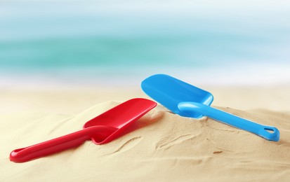 Image of Red and blue plastic toy shovels on sandy beach near sea 