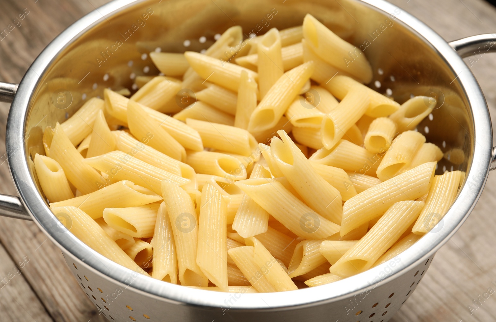 Photo of Delicious penne pasta in colander on table, closeup